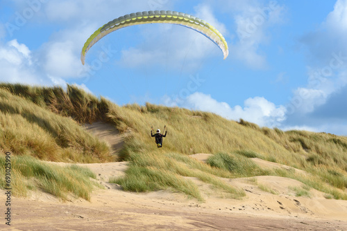 Fototapeta Naklejka Na Ścianę i Meble -  Action shot of an extreme paraglider skimming across the dunes along a beach showing amazing skill and daring