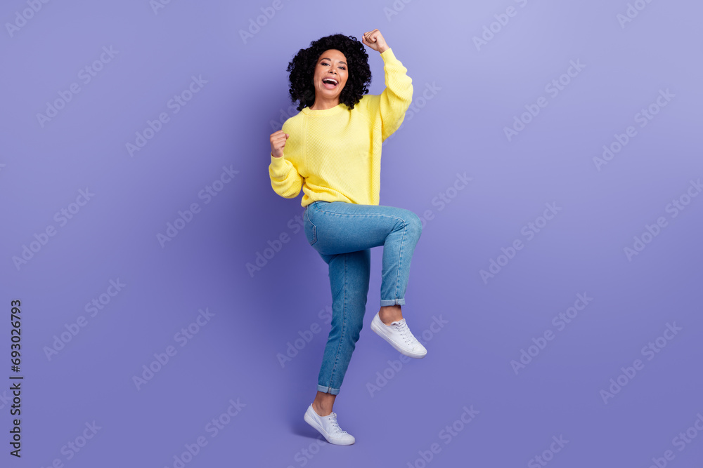 Full size photo of overjoyed woman dressed yellow sweater denim pants clenching fists win bet yell isolated on violet color background Full size photo of overjoyed woman dressed yellow sweater denim pants clenching fists win bet yell isolated on violet color background
