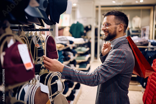 Happy man looking for a knitted hat while shopping in clothing store at mall.