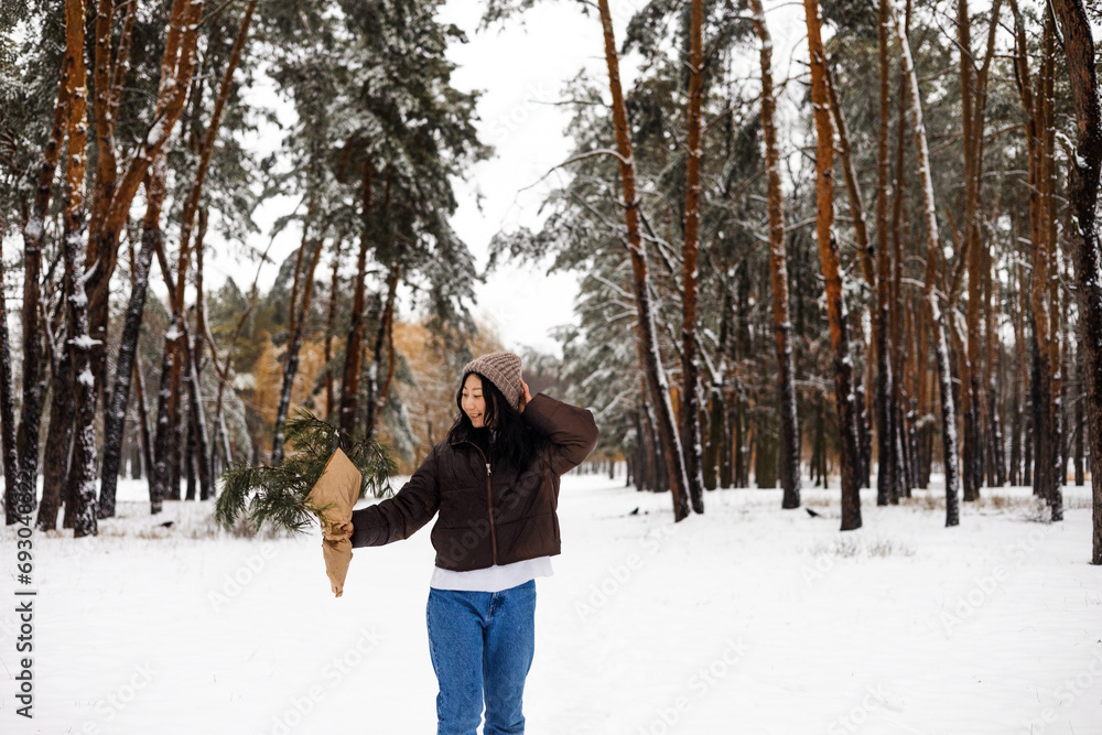 Young Asian woman holding Christmas tree branch enjoying winter weather in the snow forest.  holidays, rest, travel concept.