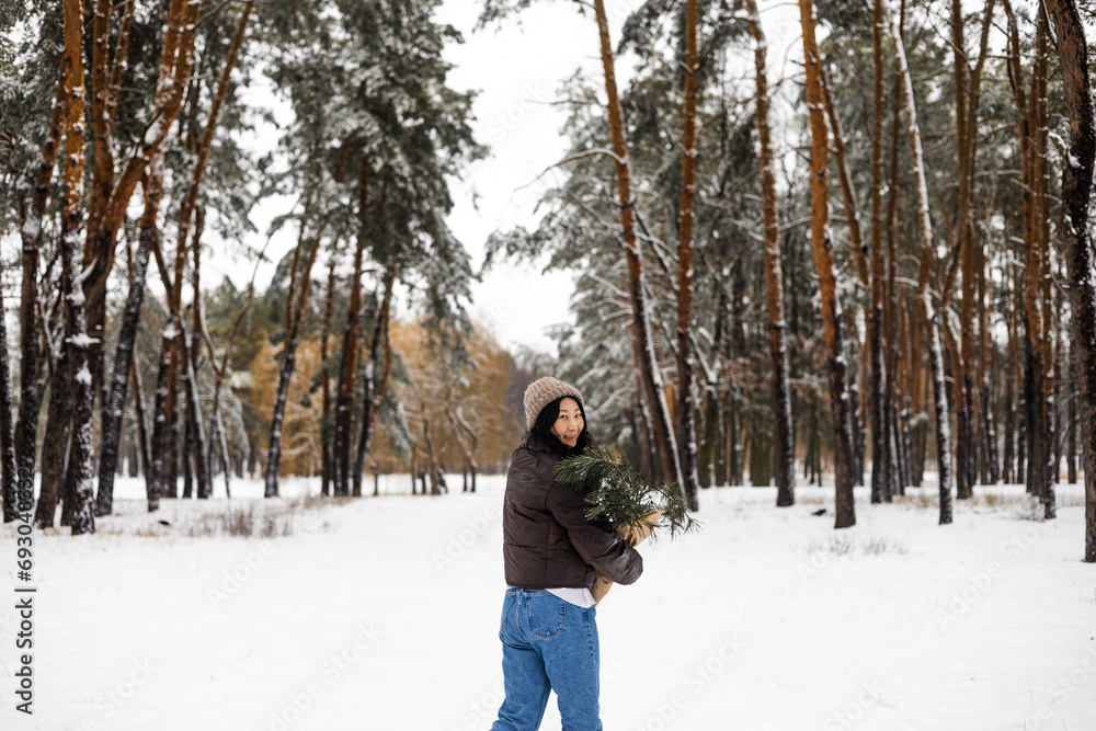 Young Asian woman holding Christmas tree branch enjoying winter weather in the snow forest.  holidays, rest, travel concept.