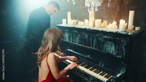 Two person fall in love Happy sexy couple play the piano together in four hands man and blonde woman enjoy romantic date. girl musician red dress bare sexy back. Guy Fashion model. dark night room. 4k photo