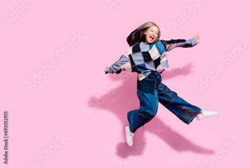 Full size photo of ecstatic active girl dressed jeans pullover oversize pants jumping fooling around isolated on pink color background