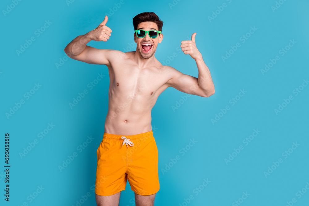 Photo portrait of nice young male excited showing thumbs up wear trendy yellow shorts isolated on blue color background summer vacation
