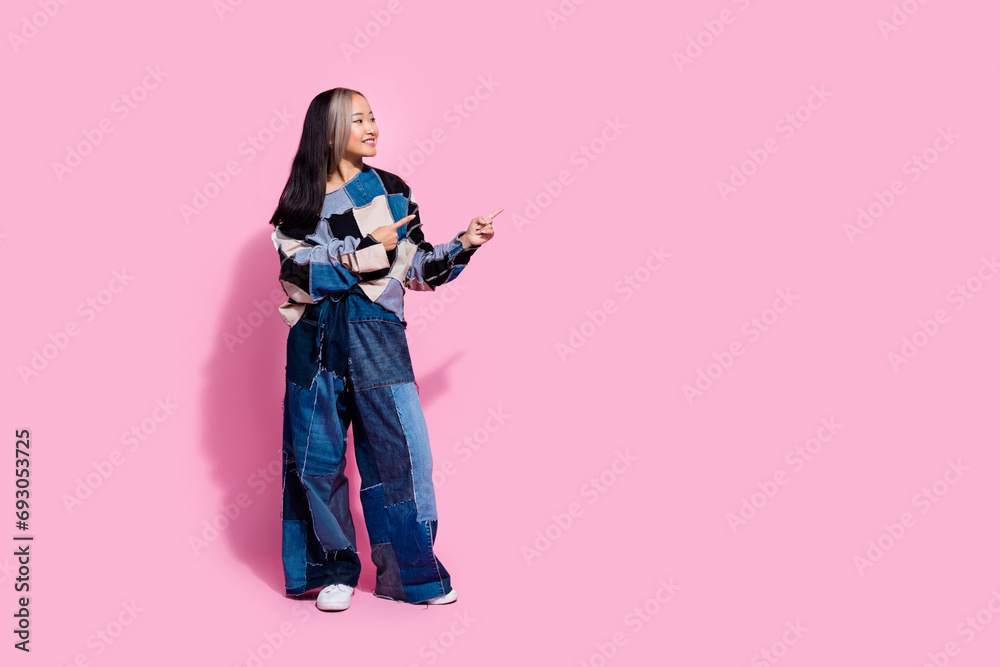 Obraz premium Full size photo of cute girl dressed jeans pullover oversize pants indicating look at offer empty space isolated on pink color background