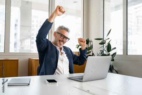 Enthusiastic mature businessman is clenching hands into fists, a happy senior business owner scream yes with triumph, having received great news of good deal, celebrating success of completed project photo