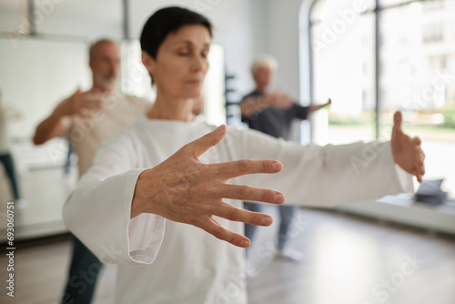Medium shot with focus on hand of senior female student doing qigong concentration exercise in gym photo