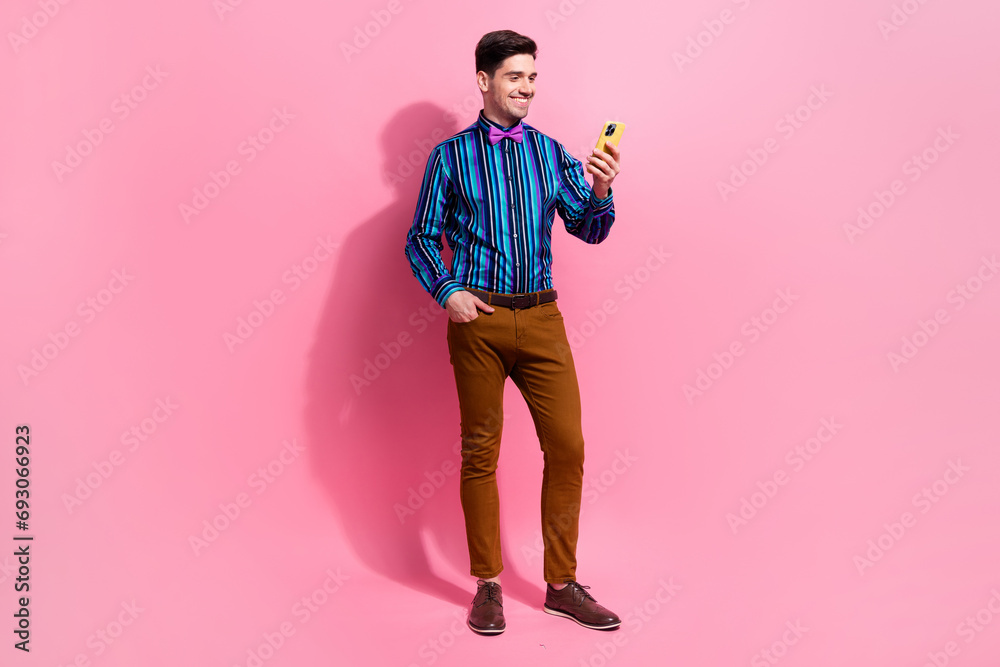 Fototapeta premium Full body length photo of handsome young funny positive man browsing smartphone take his device to chat isolated on pink color background