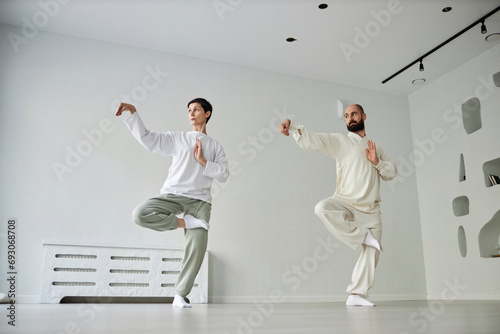 Full length shot of qigong male master and brunette mature woman standing in crane position balancing on one leg