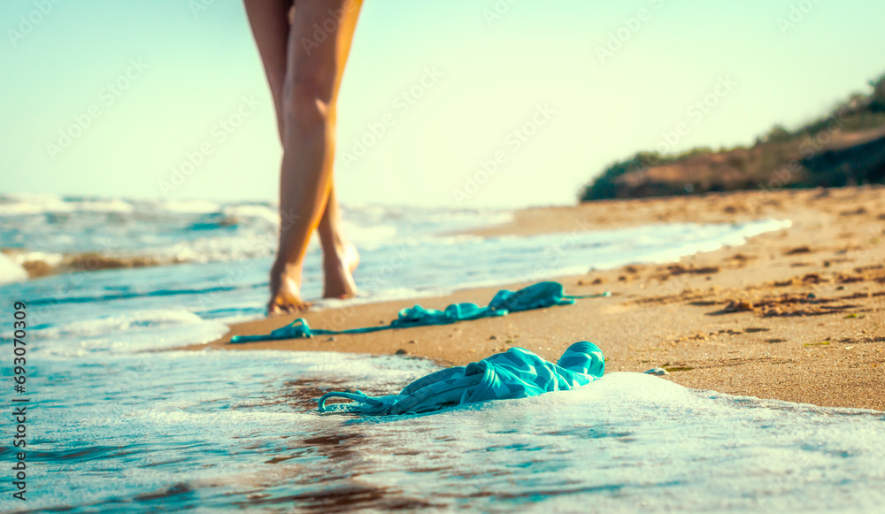 swimsuit in the sand on the beach near the sea surf on the background of a naked female figure and blue sky - obrazy, fototapety, plakaty 