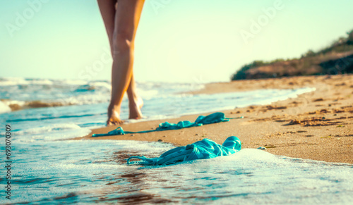 swimsuit in the sand on the beach near the sea surf on the background of a naked female figure and blue sky