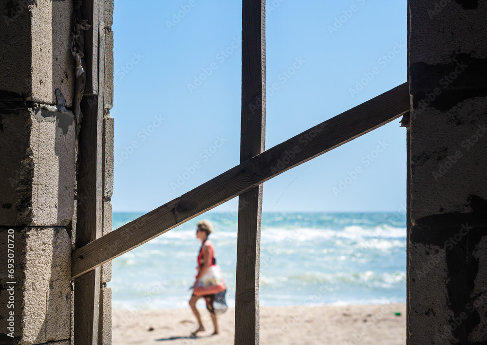 cross of boards in the window overlooking the sea, the beach and the outgoing girl