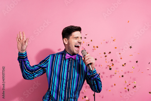 Photo of excited overjoyed person hold microphone sing flying stars confetti isolated on pink color background photo