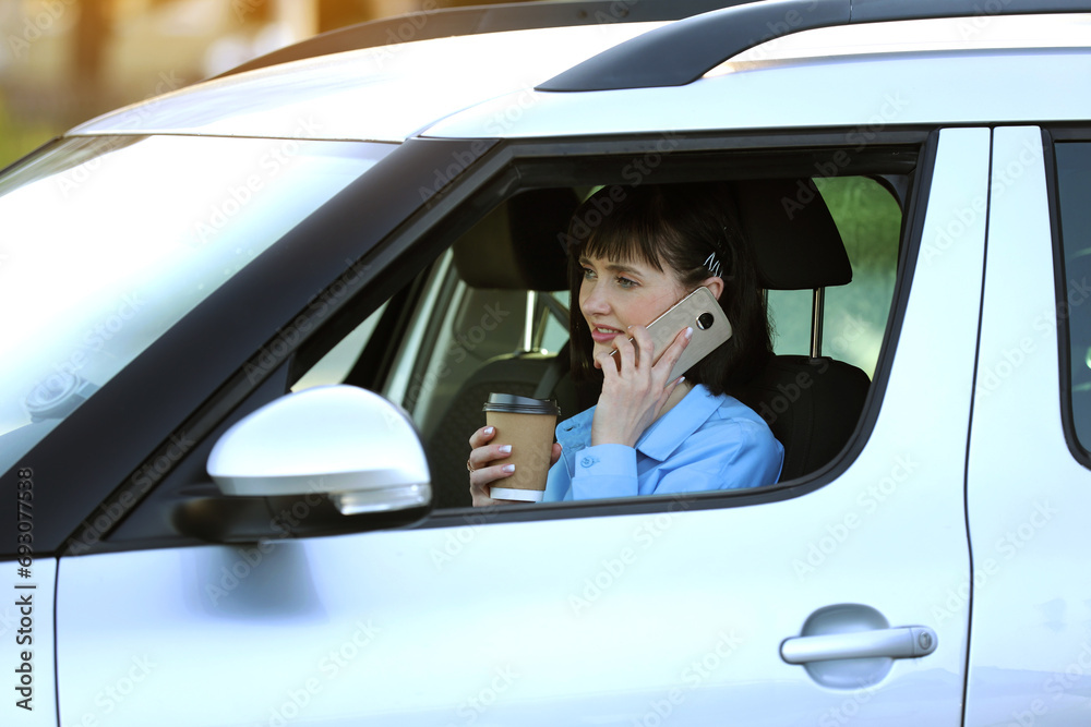 Remote work. Successful businesswoman entrepreneur holds paper cup of coffee while talking on smartphone in comfortable car. Work on road in the midst of traffic jams. Concept of results orientation