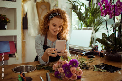 Young woman florist using smartphone in flower store photo