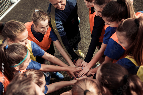 Female soccer team putting hands together with coach photo
