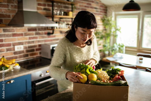 Woman taking vegetables out of cardboard box in kitchen at home photo