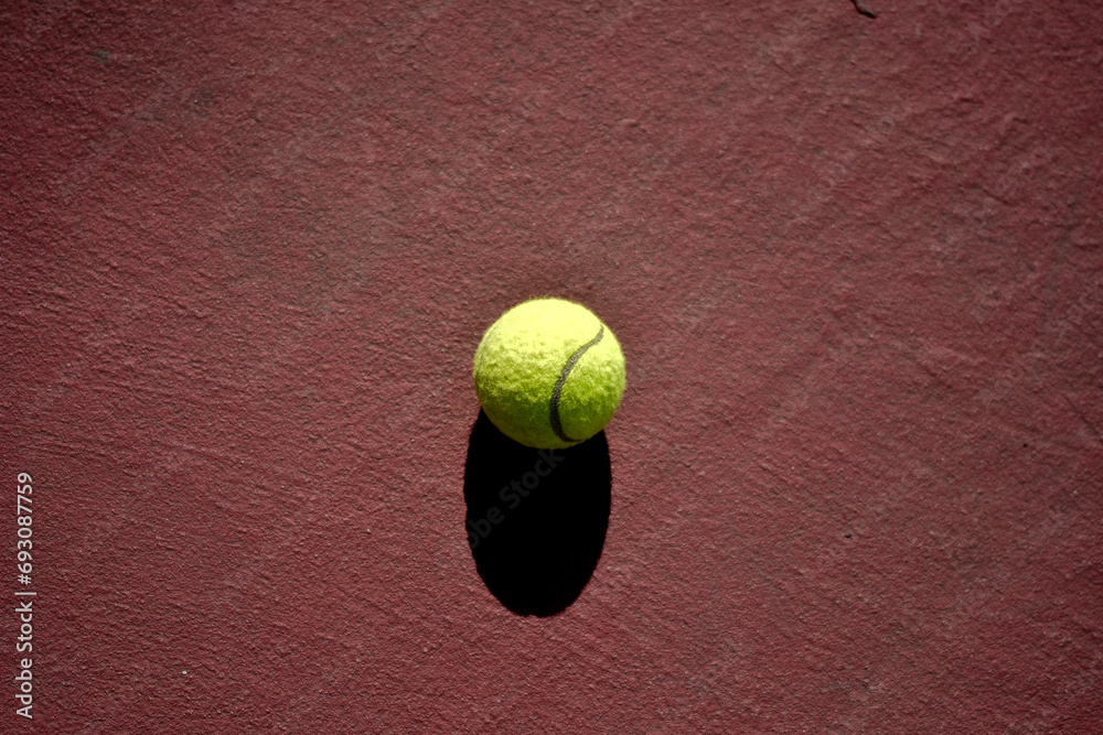 Tennis ball with black shadow on red court