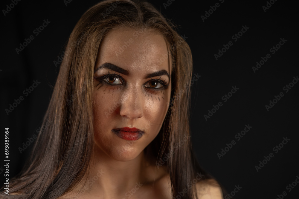 Halloween. Portrait of a beautiful woman in the style of a gothic witch on a black background. On Halloween, the witch stands in the dark and stares into the camera. Halloween holiday concept.