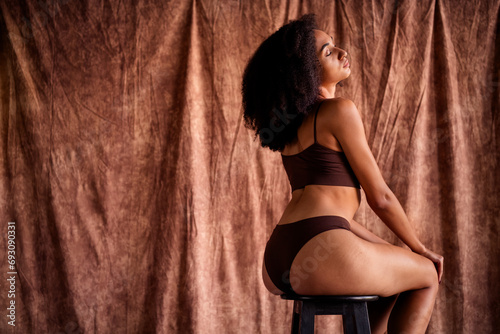 Photo portrait of pretty lovely young girl no filter sit chair show back booty dressed brown underwear isolated on studio fabric background