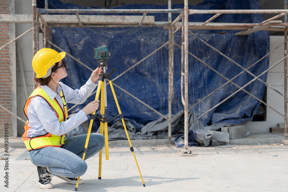 Fototapeta premium Civil engineer woman in vests and helmet safety wear sunglasses using laser level meter at construction site. Forman female working in building workplace.
