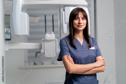 portrait of a beautiful young female doctor dentist or radiologist in uniform standing with crossed arms in the beauty and health clinic photo