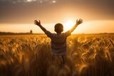 silhouette with a boy with his arms outstretched towards the sun in the sunset landscape in a wheat field

