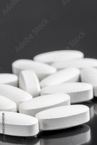White pills on a black background. Scattered pills on a dark background. Copy space. Pharmacy healthcare. Vertical orientation.