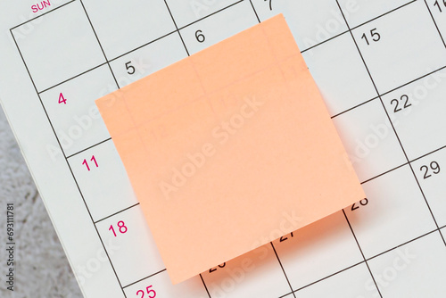 Orange paper sticky note and stuck to a calendar background. Reminder concept.