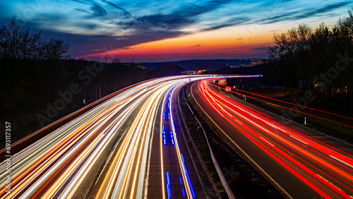Colorful panorama of German motorway A45 called “Sauerlandlinie“ with curved lanes at blue hour twilight after sunset near Hagen. Colorful light traces of passing cars and blue flash lights. photo
