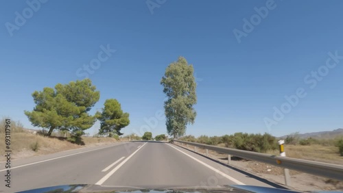 First person view, FPV, from dashcam of car driving on highway towards Valencia from Tabernas desert, Almeria, Andalusia, Spain, Europe. Road trip video in POV on beautiful tree-lined road with farms photo