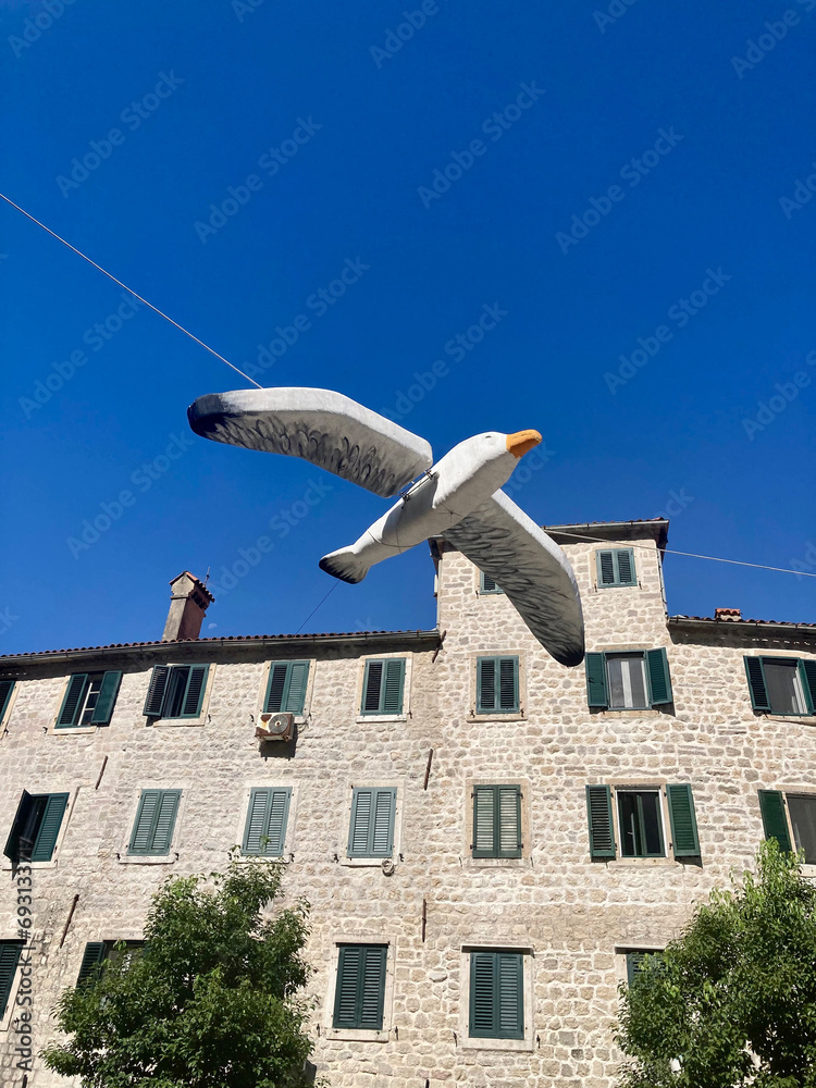 View of a large figure of a seagull. In the background is an old building and a clear, clear and blue sky View of a large figure of a seagull. In the background is an old building and a clear, clear and blue sky