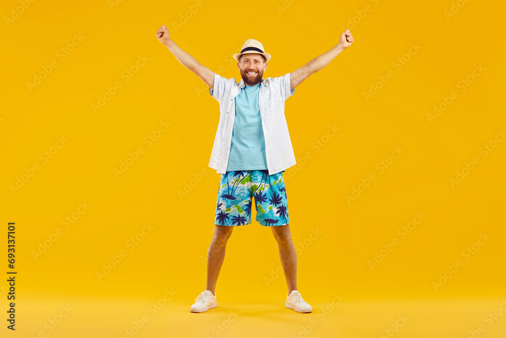 Full body photo of young happy man standing with hands up in fists wearing summer casual clothes and white sneakers isolated on yellow studio background. Portrait of smiling guy looking at camera.