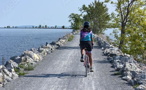 woman riding a bicycle on the colchester causeway in vermont (burlington gravel bike cycling path across lake champlain to south hero island line rail trail) cyclocross tires, from behind (no face) photo
