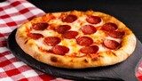 Pepperoni pizza on black board, text space top wiev. Red and white checkered tablecloth