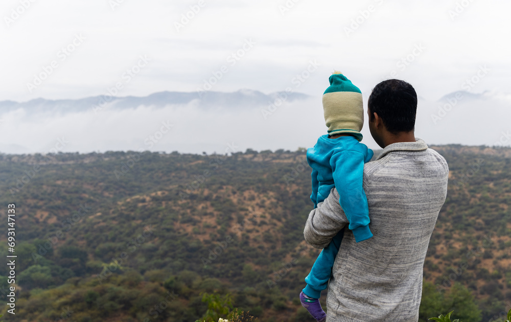 Naklejka premium father holding son infant in arm and showing him the amazing mountain landscape at morning