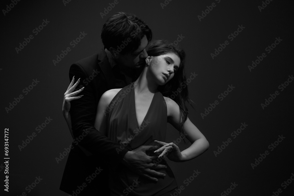 A passionate portrait of a man in a black suit and a woman in a red dress on a dark background, black and white photo.