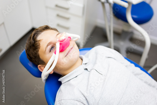 Fear of the dentist! A little boy sits in a dentist's office wearing a nasal mask to breathe nitrous oxide to relax. Concept of feeling relaxed with laughing gas. photo