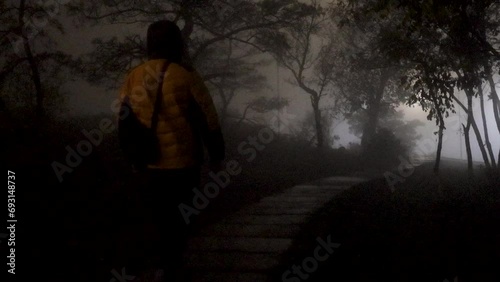 A solitary man in a vibrant orange hooded jacket strolls serenely along a wet winding pathway on a misty evening, heading away from the camera, with cars subtly moving in the misty background, uhd, 4k photo