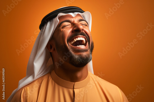 Portrait of happy Saudi young man smiling opening his mouth with joy standing over yellow orange background. photo