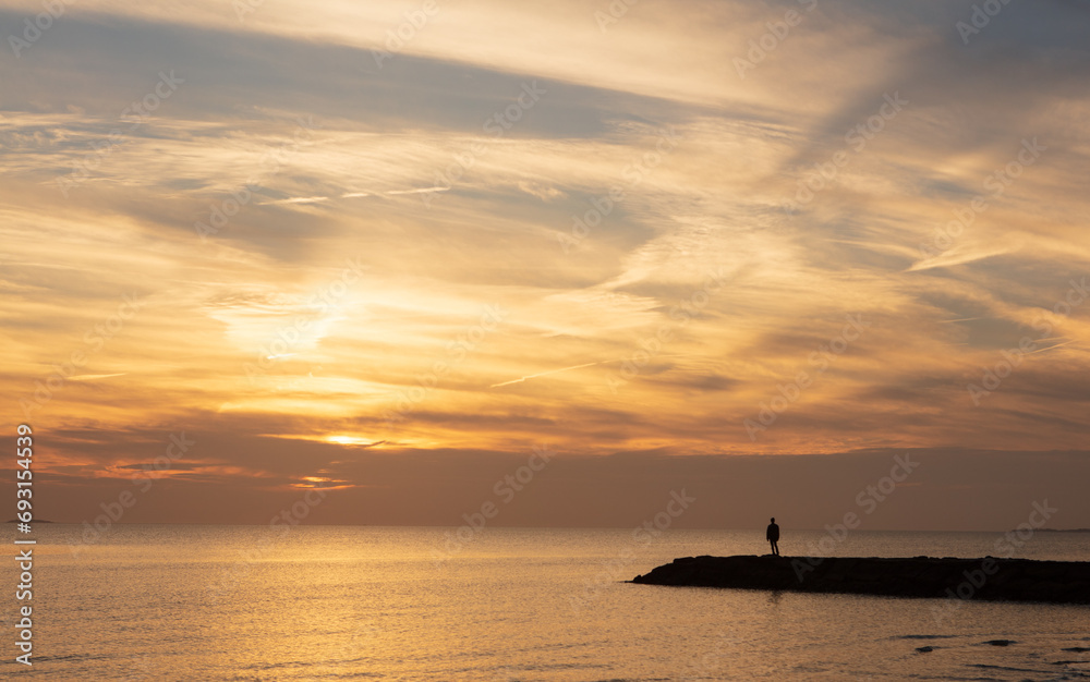 A silhouette of a man standing on a jetty looking at the sunset.