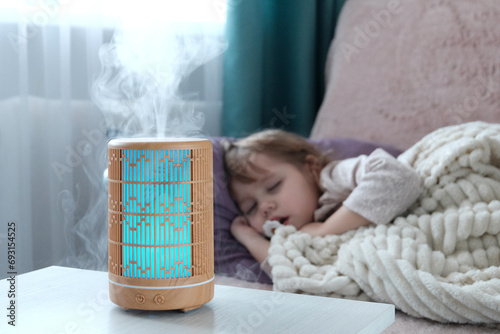 Wooden diffuser, blue light, electric aromatic. A little blonde girl is resting on the sofa. The concept of care and comfort, air humidification in the house.