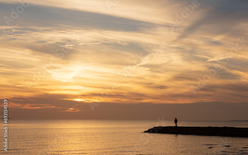 A silhouette of a man standing on a jetty looking at the sunset. © kmlPhoto