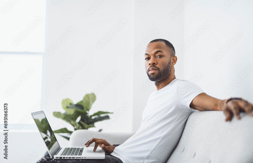 Young happy man on laptop at home A Casual guy sitting on couch in light livingroom Young happy man on laptop at home A Casual guy sitting on couch in light livingroom
