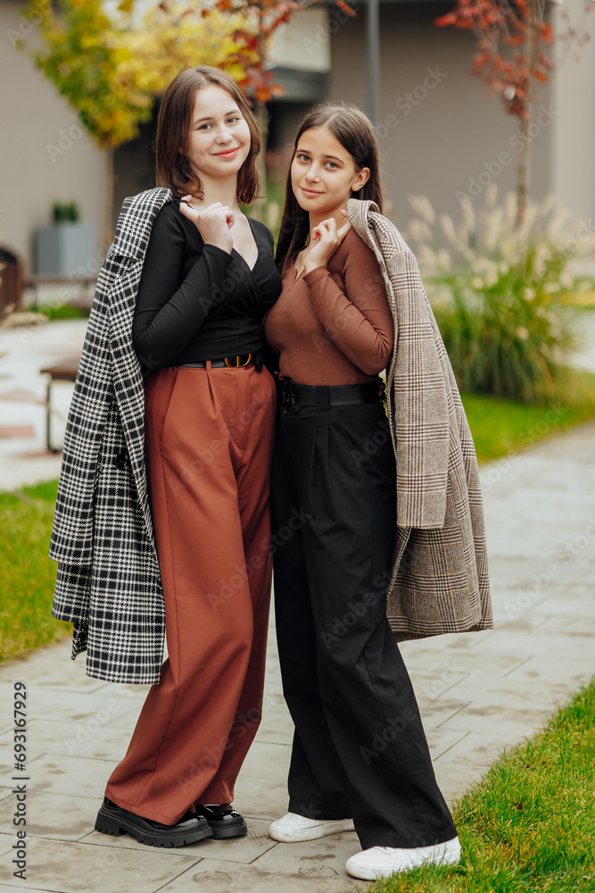Vertical photo of two teenage friends dressed in casual clothes standing next to each other against a background of nature. Best school friends are ready to overcome anything to achieve the goal. Vertical photo of two teenage friends dressed in casual clothes standing next to each other against a background of nature. Best school friends are ready to overcome anything to achieve the goal.
