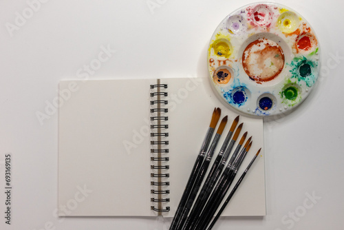 Open spiral notebook with watercolor palette and brushes on white background with copy space