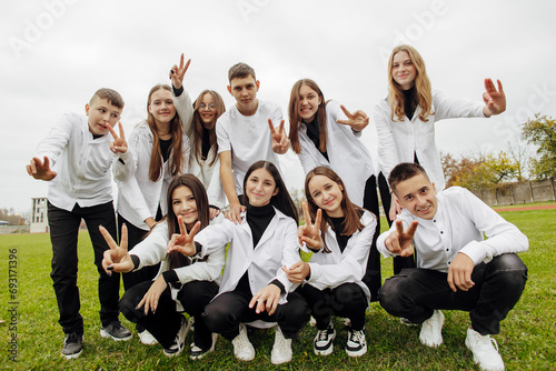 A group of many happy teenagers dressed in the same outfit having fun and posing in a stadium near a college. Concept of friendship, moments of happiness. School friendship photo