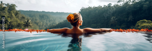 Woman with flowers in hair relaxing in Infinity pool with a view to the jungle.	
 photo
