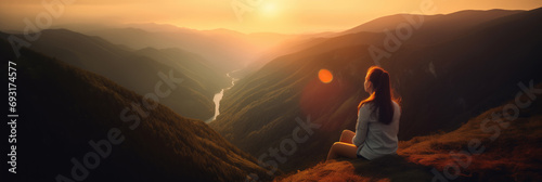 Young woman sitting on a ledge of a mountain and enjoying the beautiful sunset over a wide valley.  photo