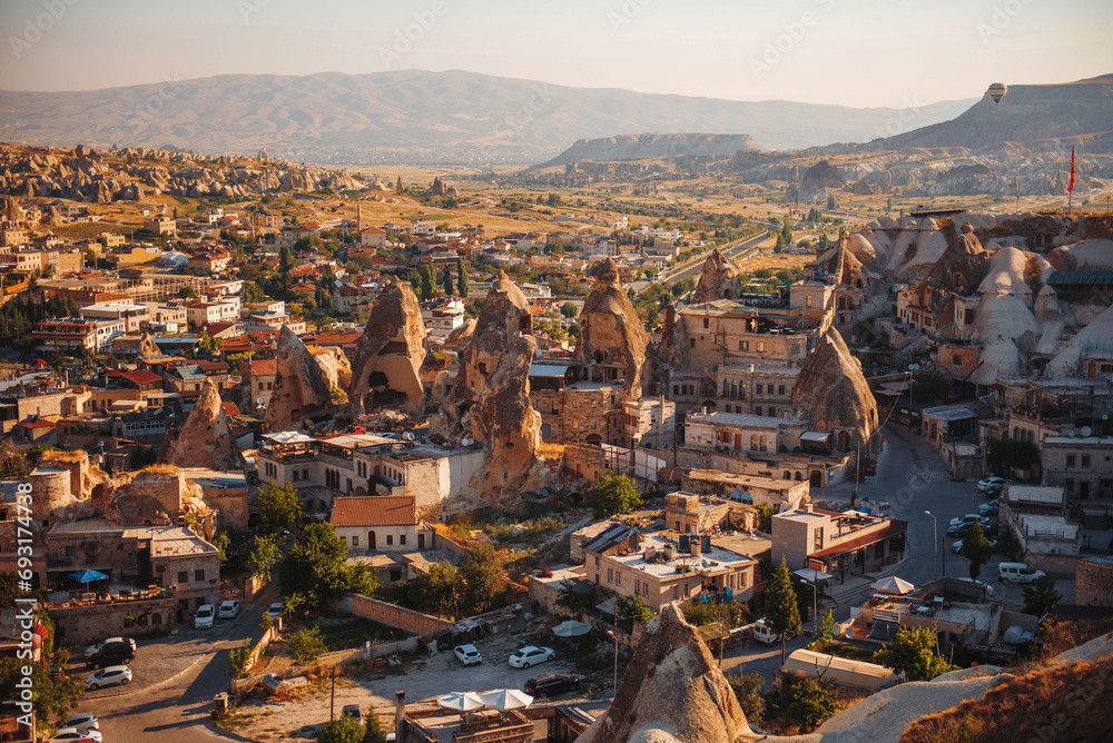 Top view of beautiful small town in Turkey surrounded with rocky mountains. Air Balloons flying in Cappadocia region. Concept of adventure and travelling.